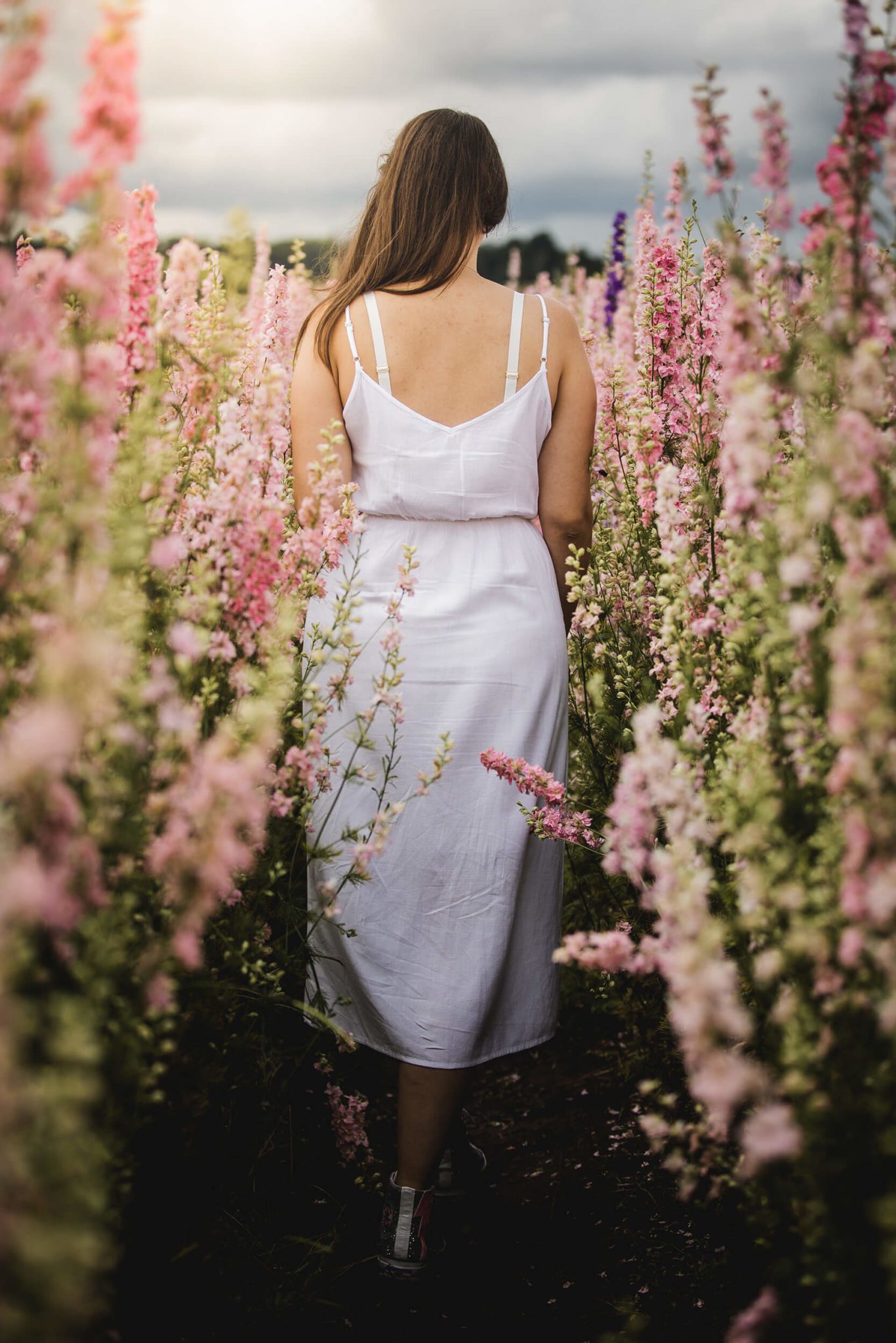 Woman in white dress walking away from camera in a field of pink delphiniums